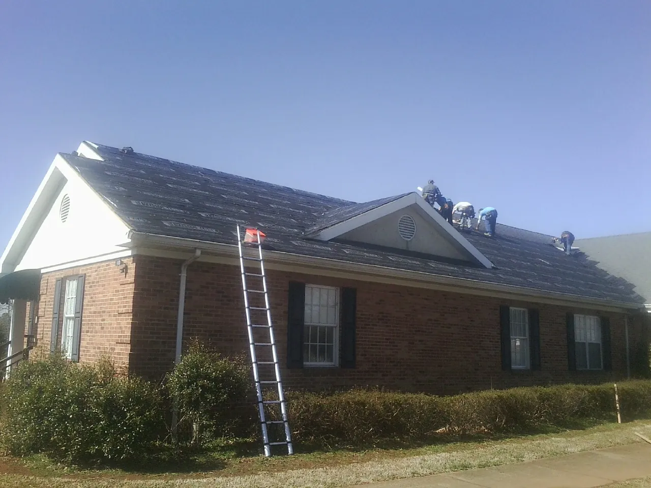 Crew tearing shingles off a brick ranch roof with a ladder set — Metal Roof Repair work by our crew in Loganton