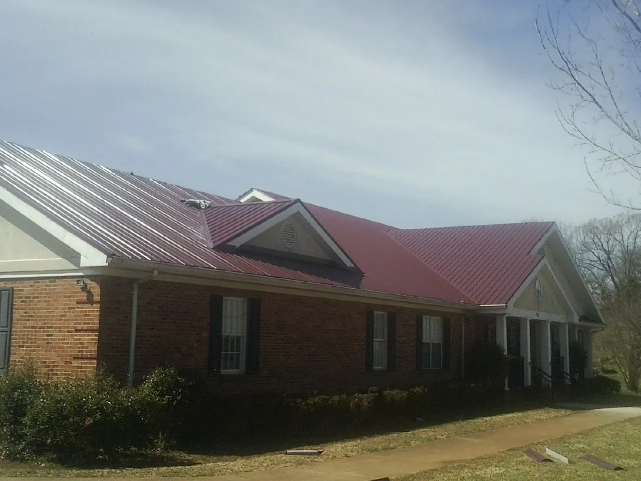 Red metal roof with gabled entries on a long brick building, from a Hail Damage Roof Repair job in Loganton