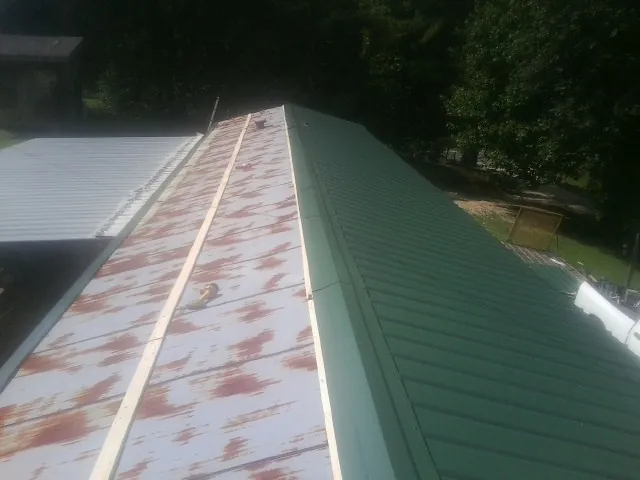 Old rusted panels beside newly installed green metal roofing — Wind Damage Roof Repair by Roofing Brothers in Loganton