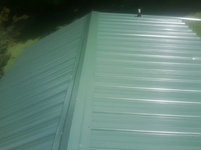New green metal panels meeting at the ridge of a roof — Flat Roof Repair work by our crew in Loganton