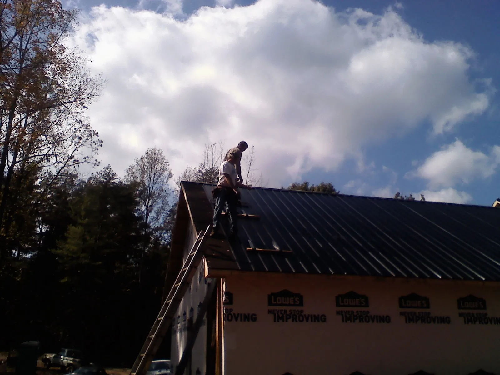 Roofer fastening dark metal panels high against a cloudy sky, from a Roof Inspection job in Loganton